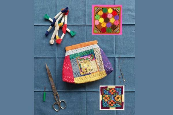 Buntes, besticktes Täschchen, umgeben von Stickgarn, Schere und Stickmustern