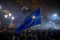 Menschenmenge bei Nacht mit wehender Europaflagge vor einem beleuchteten historischen Gebäude