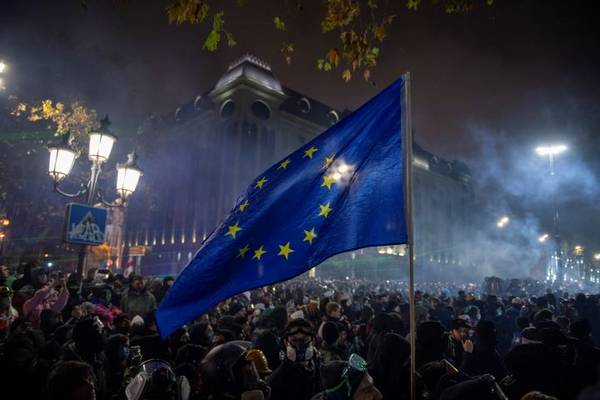 Menschenmenge bei Nacht mit wehender Europaflagge vor einem beleuchteten historischen Gebäude